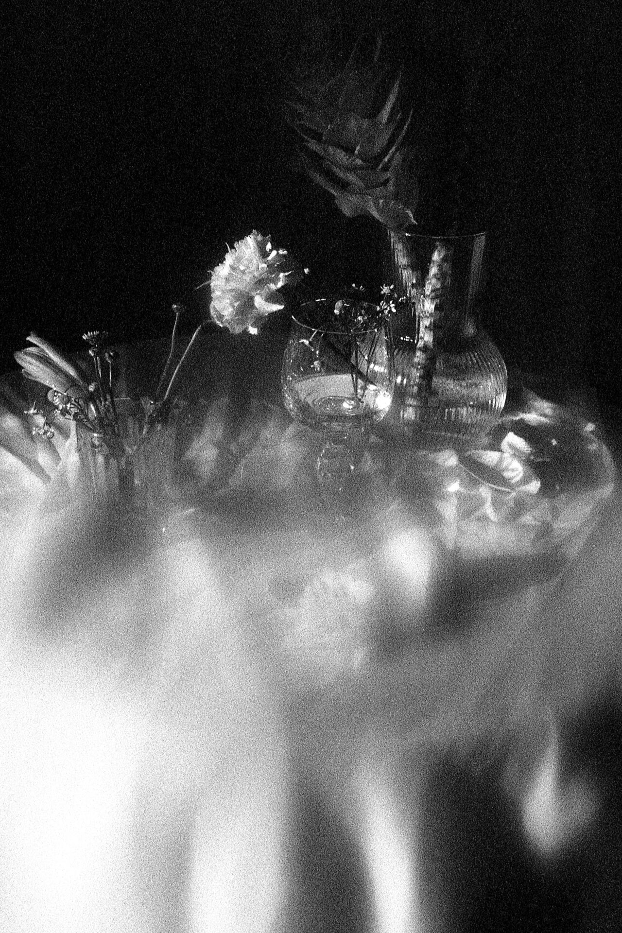 Schwarzweiß-Stillleben mit Blumen und Glasvasen auf einem runden Tisch. Analoge Fotografie